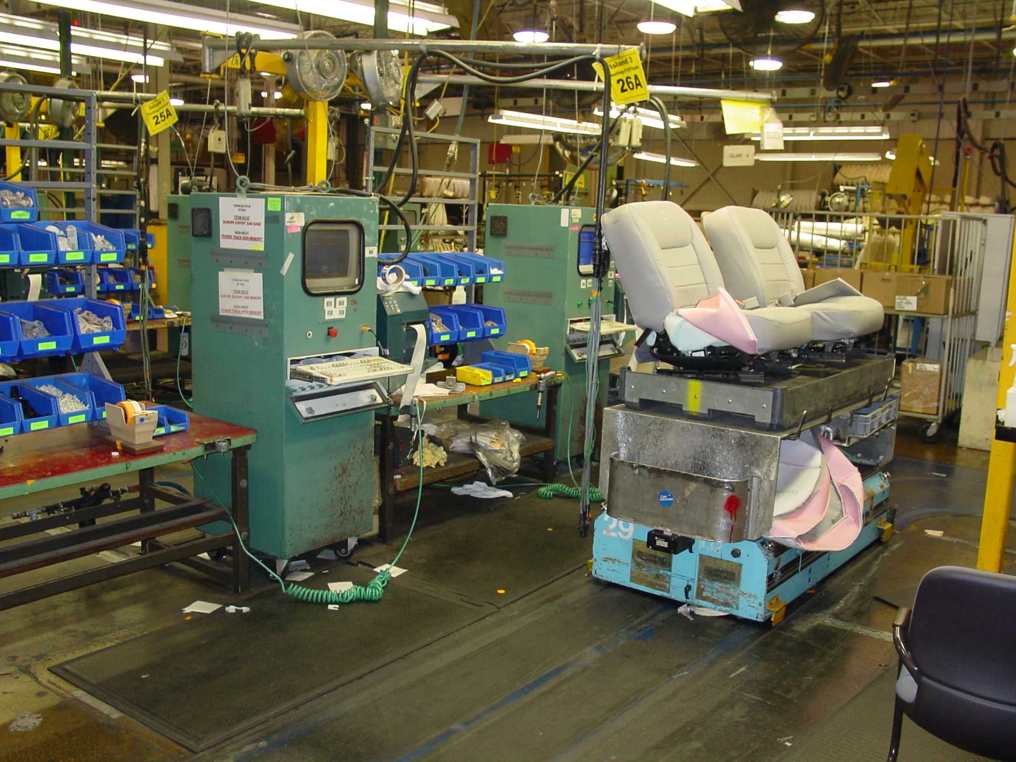 Seat tester carrier #29 mid-test — operator station with the original-era CRT display, seat backs visible, surrounding parts bins and the broader assembly floor in frame