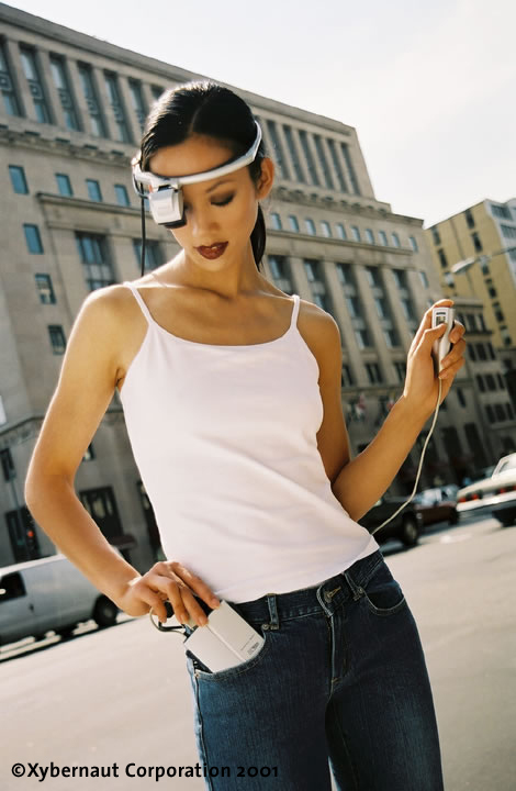 Same Xybernaut POMA consumer wearable in use, second angle — the operator looking down at the belt-mounted unit with the pen-input controller in hand. 2001-era Xybernaut Corporation press photo of the Poma product line.